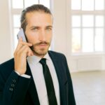 Confident businessman in formal suit taking a phone call in a well-lit modern office.